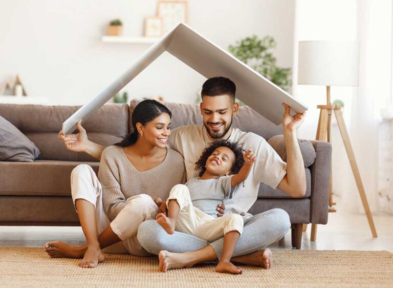 A family reviews house plans together in a bright living room with paperwork, pens, and a laptop on the table.